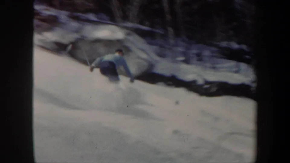 1962 Vermont 8mm frame showing a distant skier in a light sweater turning down a snowy wooded slope.
