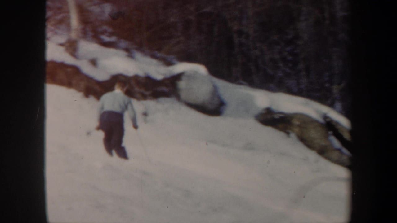 Distant skier on a Vermont snowy hillside in 1962 home-movie footage, with bare trees and rock outcrops behind.