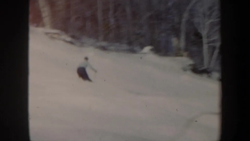 Distant 1962 Vermont skier turning across an open snowy slope with leafless trees at the edge of frame.