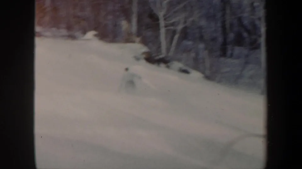 1962 Vermont 8mm frame with a distant skier crossing a snow-covered slope near leafless trees.