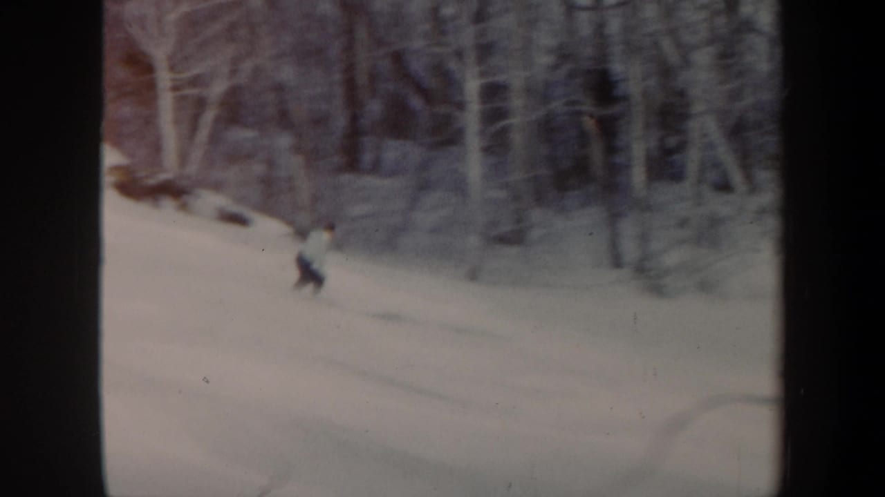 Skier in a light top and dark pants descending a snowy slope.