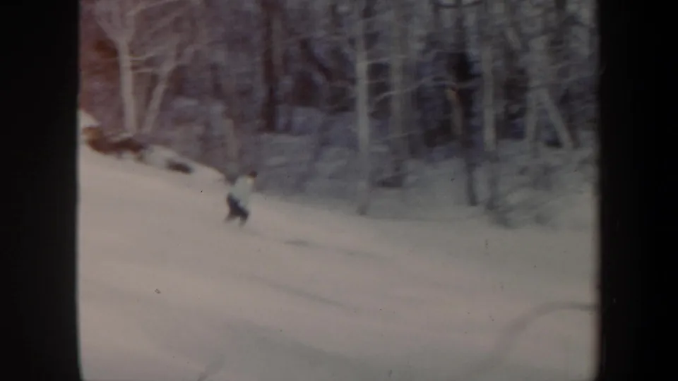 1962 Vermont home-movie frame showing a lone skier descending a snowy hillside with trees behind.