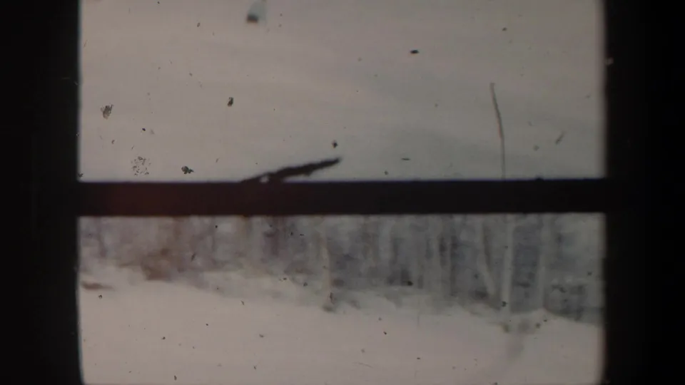 1962 Vermont 8mm frame of the snowy slope after the skier has nearly left view, with bare trees and visible film marks.