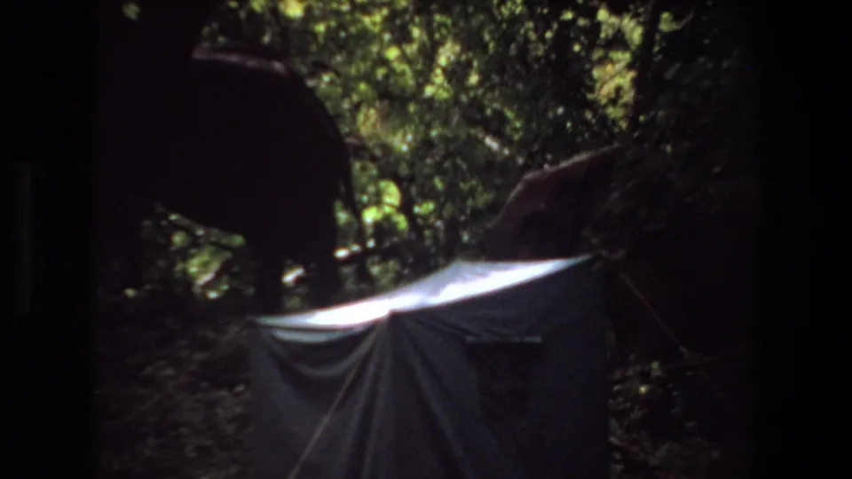 1969 Angola home-movie frame with an elephant moving behind or beside a small tent in thick greenery.