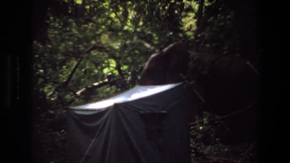 1969 Angola home-movie frame showing the tent from another shaded angle, with leafy forest growth behind and above it.
