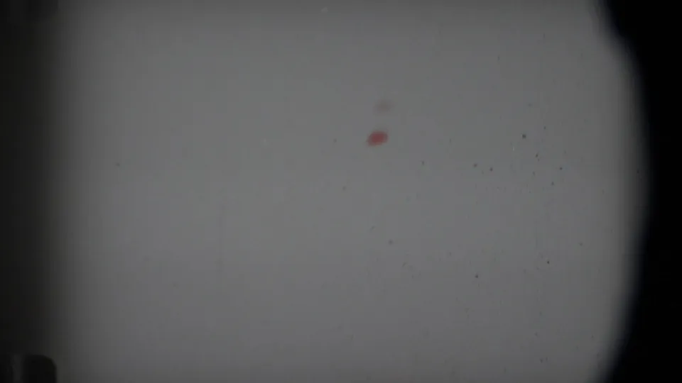 1969 Angola Super 8 roll-end frame showing pale blank film, dark gate edges, scattered dust, and a small red processing mark.