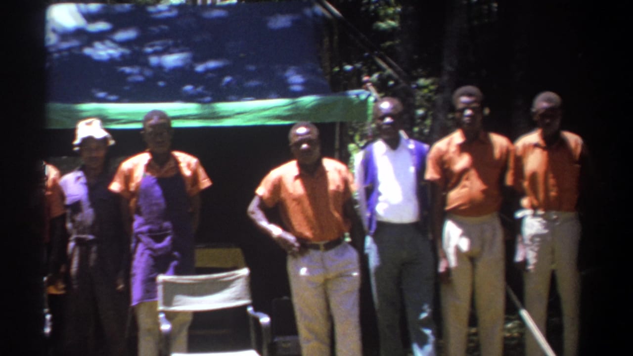 Group of adult men poses outdoors in front of a shaded tarp and trees.