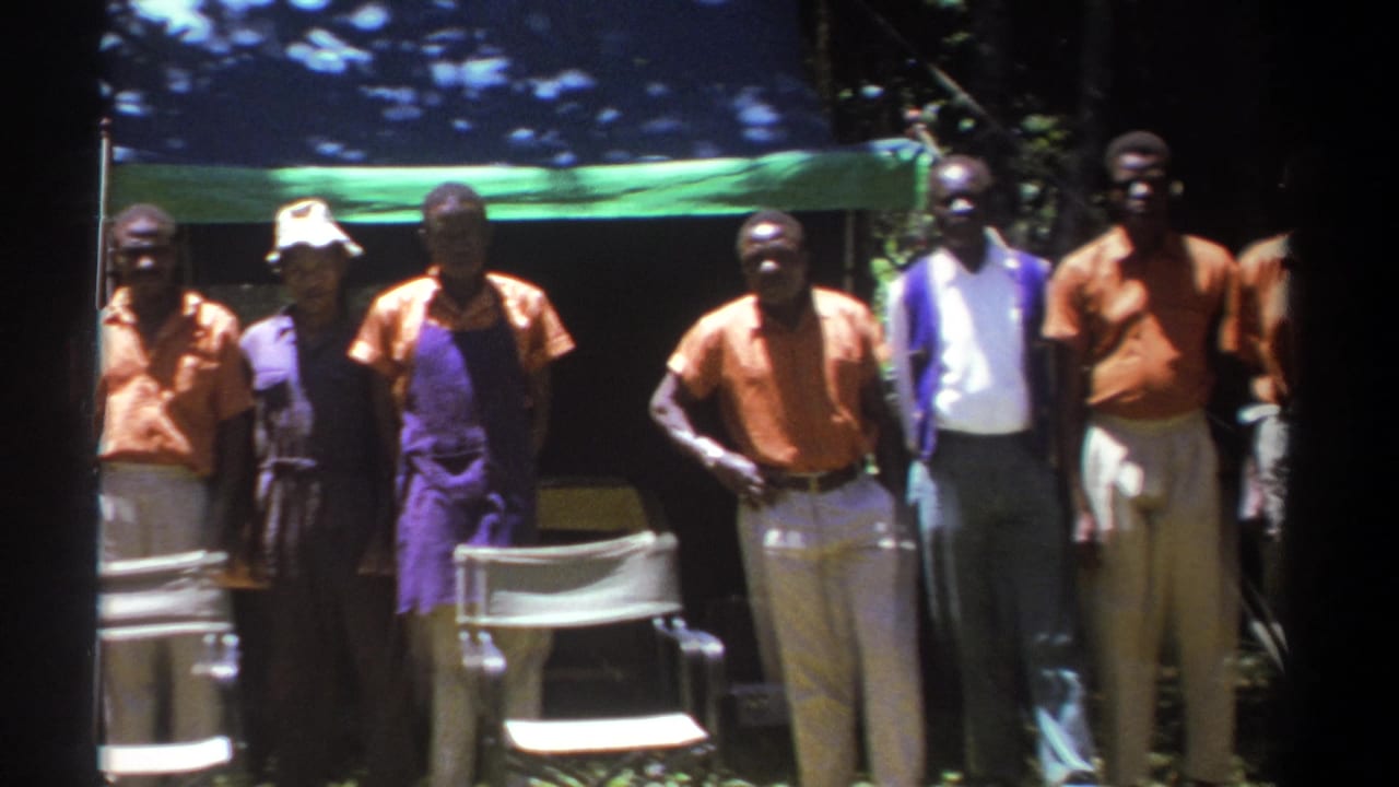 Men stand near a tent while one person in a light hat appears near the center.