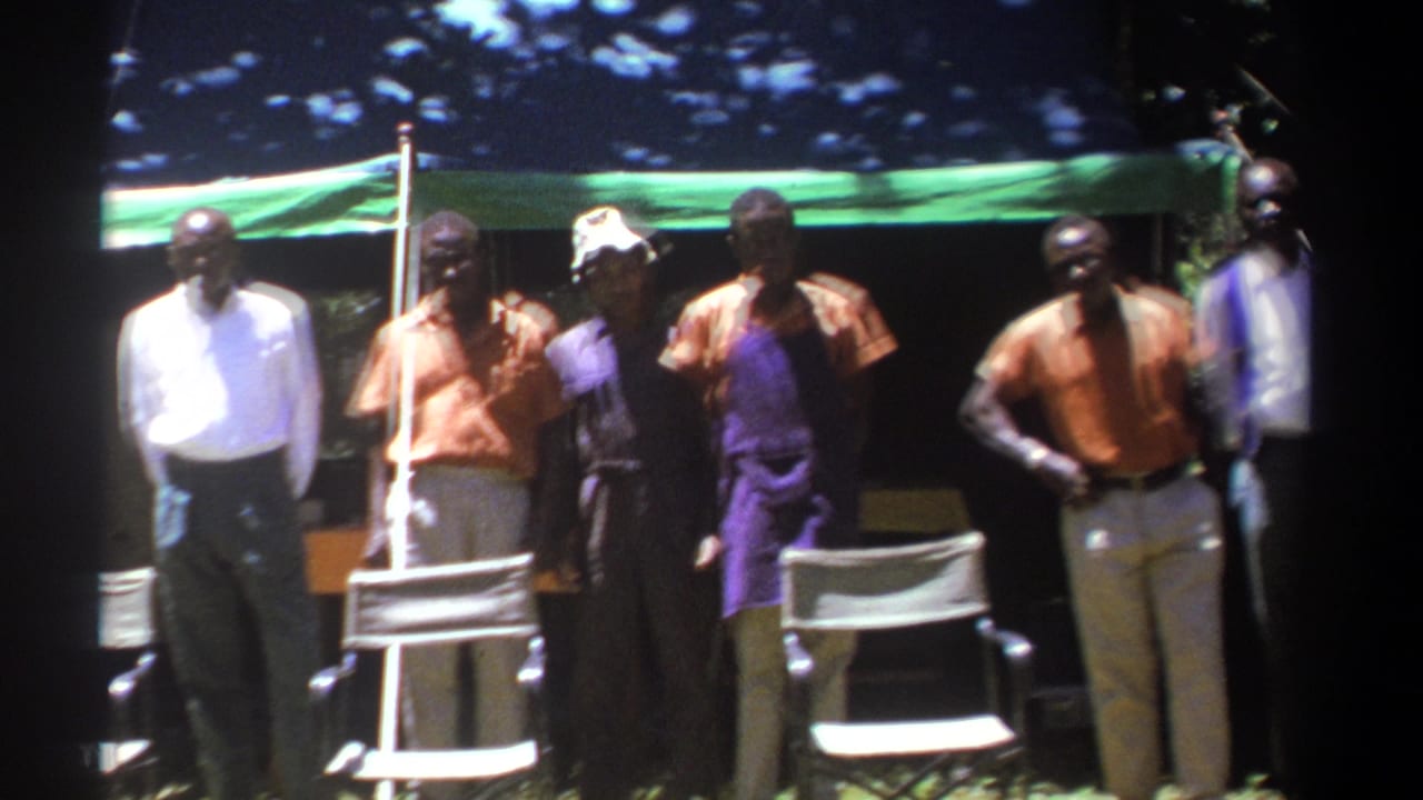 1969 Kenya 8mm frame showing men loosely arranged before a tent, with soft focus and bright sun patches across the scene.