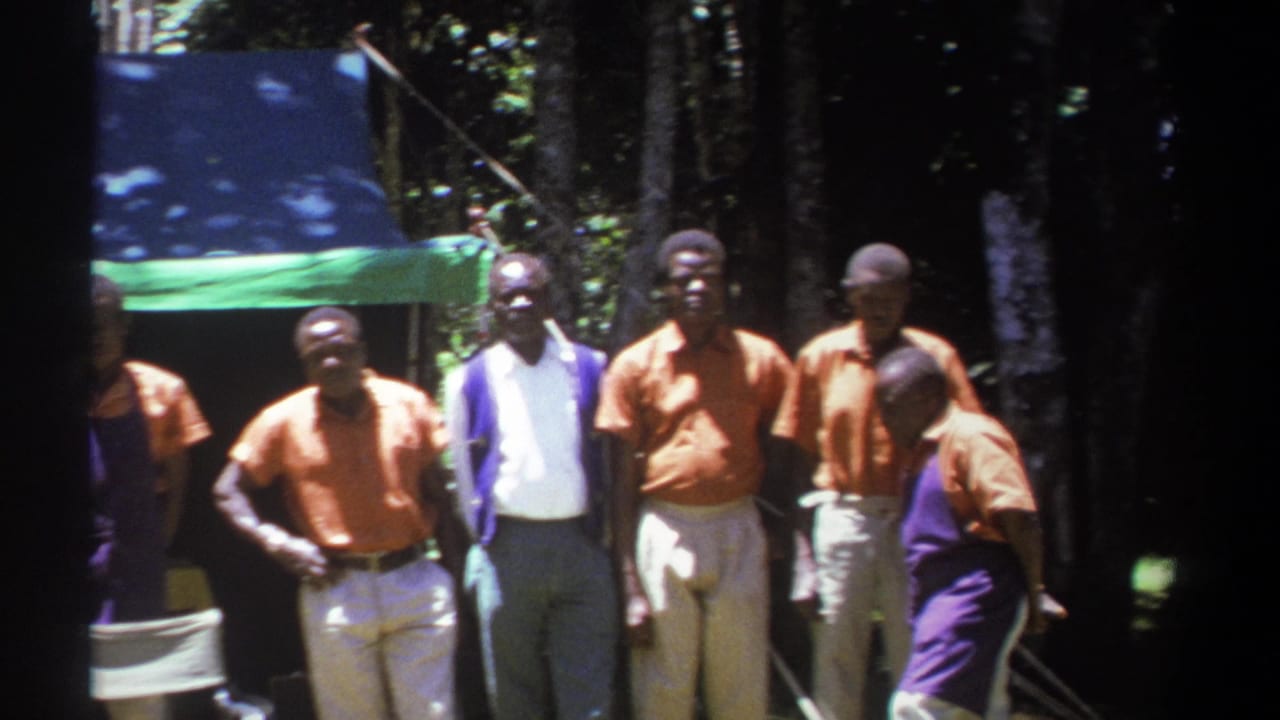 1969 Kenya frame with men grouped near a tarp in a wooded area, including one person turning sideways at the right edge.