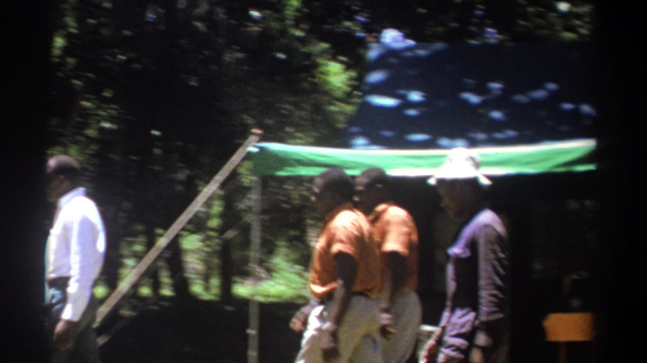 1969 Kenya 8mm frame showing several men near a green canopy tent under trees at a shaded campsite.