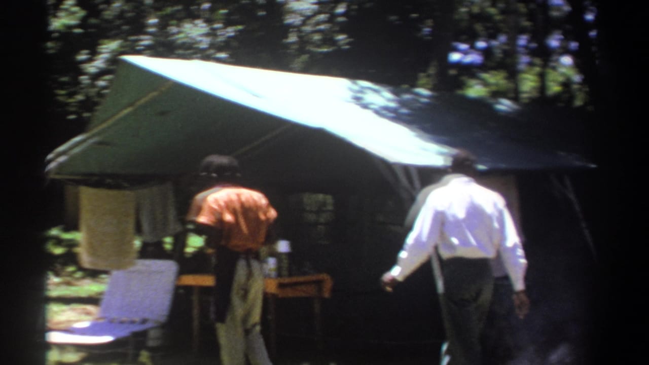 1969 Kenya 8mm frame showing men near a green canopy tent, folding chair, and towel in a wooded camp area.