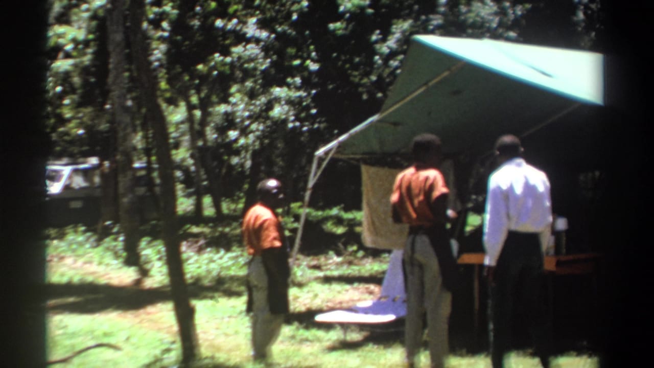 1969 Kenya 8mm frame showing several men near a green canopy tent at a forest campsite, with a vehicle partly visible through trees.