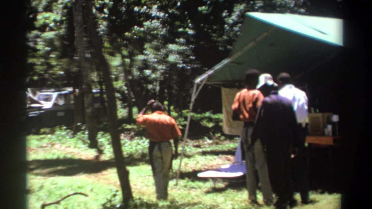 A man in an orange shirt walks toward others gathered by a canopy tent.