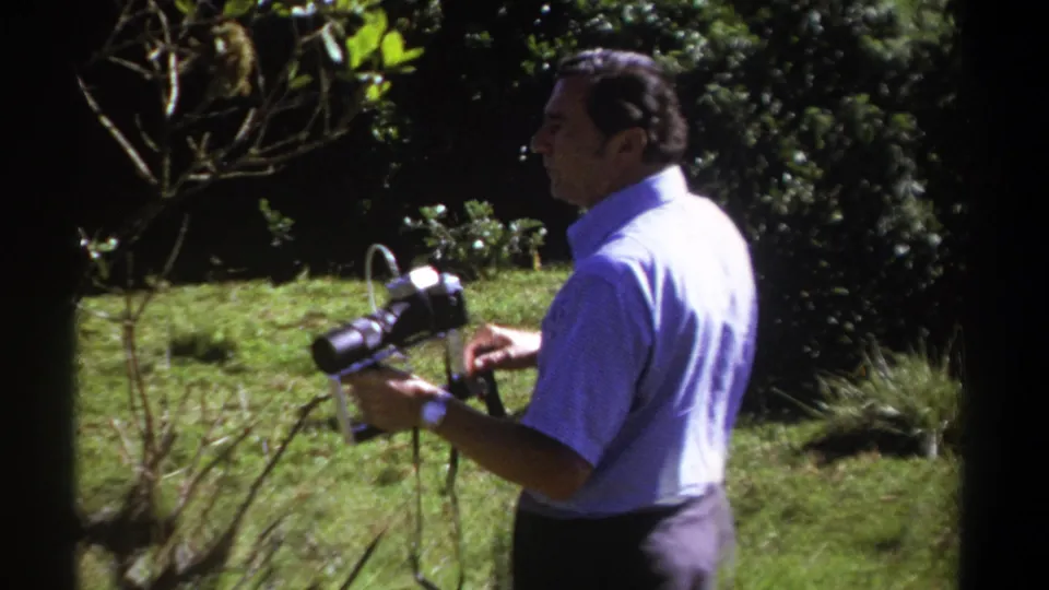 A side view shows the adult camera operator in Kenya, 1969, holding an 8mm camera in a green outdoor setting.