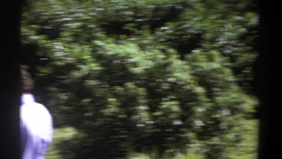 A blurred handheld 8mm frame shows green foliage and a partial view of the man at the lower edge during the 1969 Kenya scene.