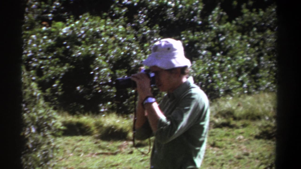 The man continues photographing nature in 1969 Kenya, framed by dark 8mm borders and lush green vegetation.