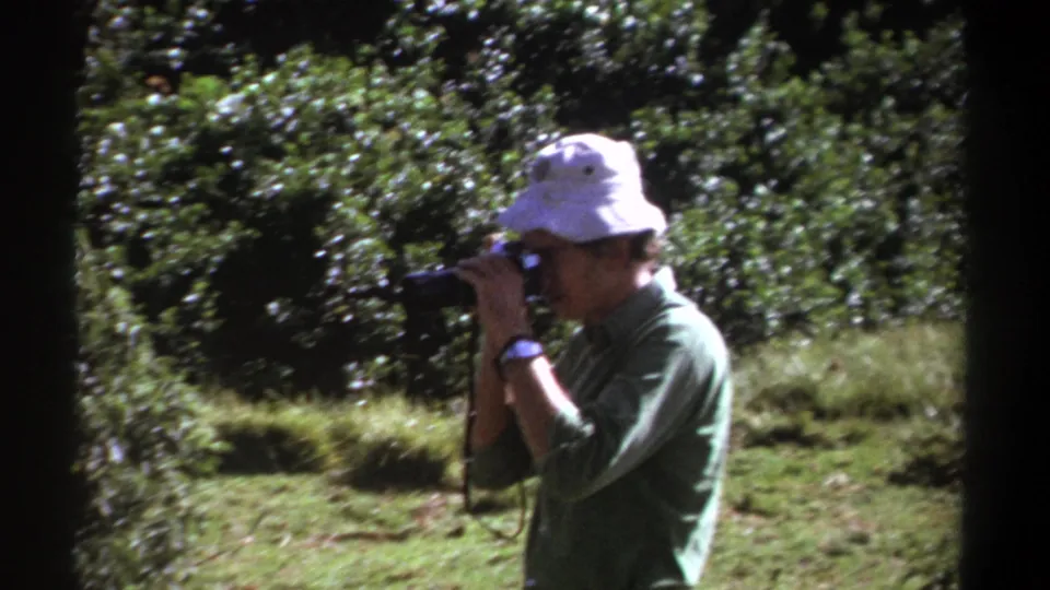 The man continues photographing nature in 1969 Kenya, framed by dark 8mm borders and lush green vegetation.