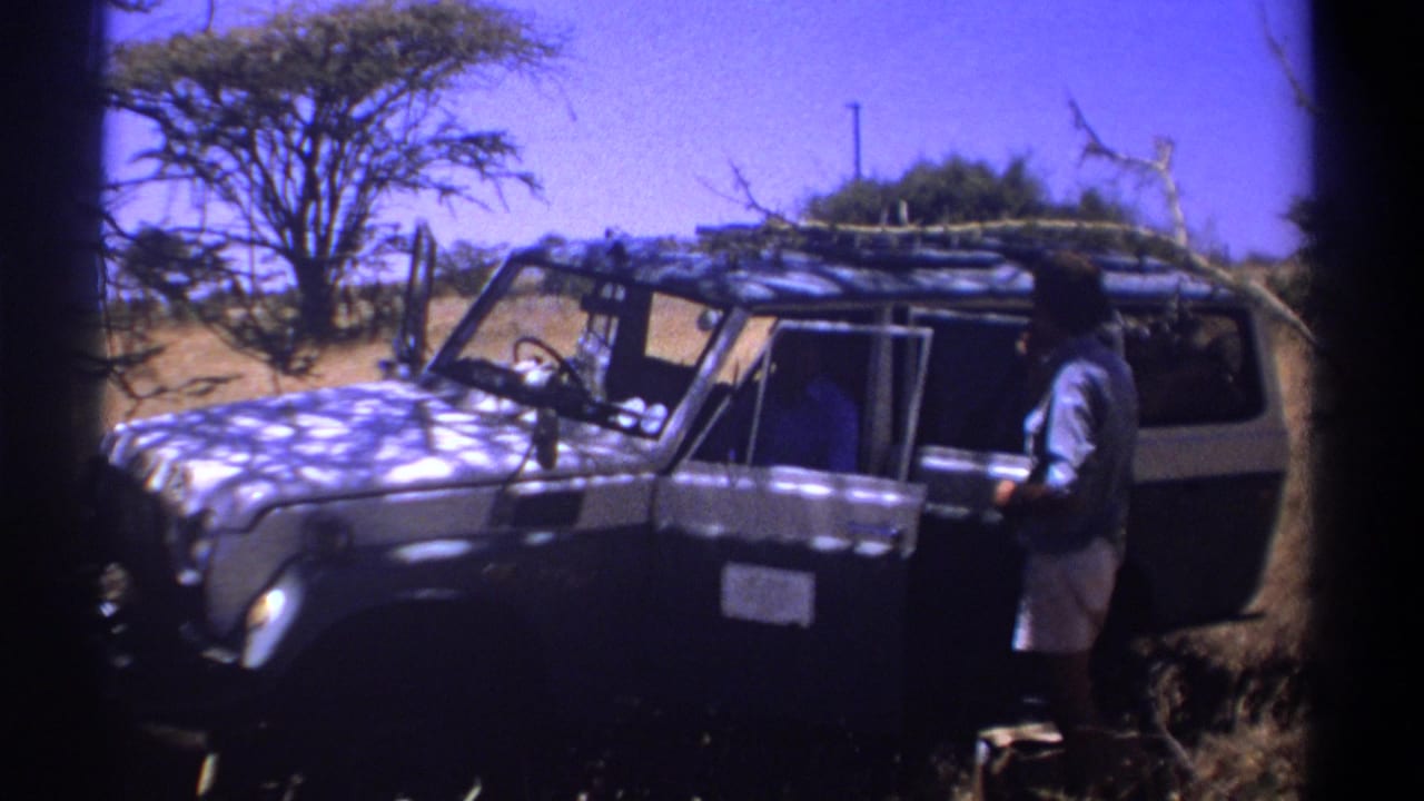 1969 Kenya 8mm frame showing a man beside an open white safari jeep with roof rack in dry grassland.