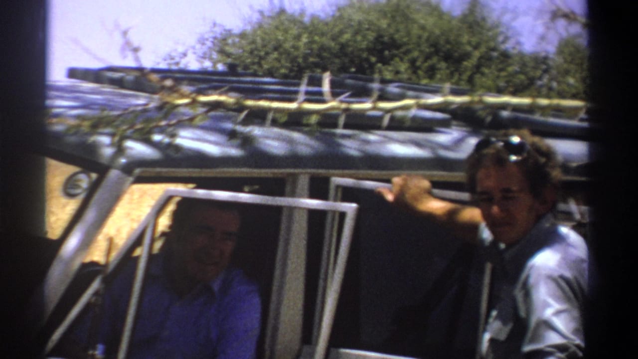 1969 Kenya 8mm frame with one man seated inside a rugged vehicle and another leaning by the passenger-side opening.