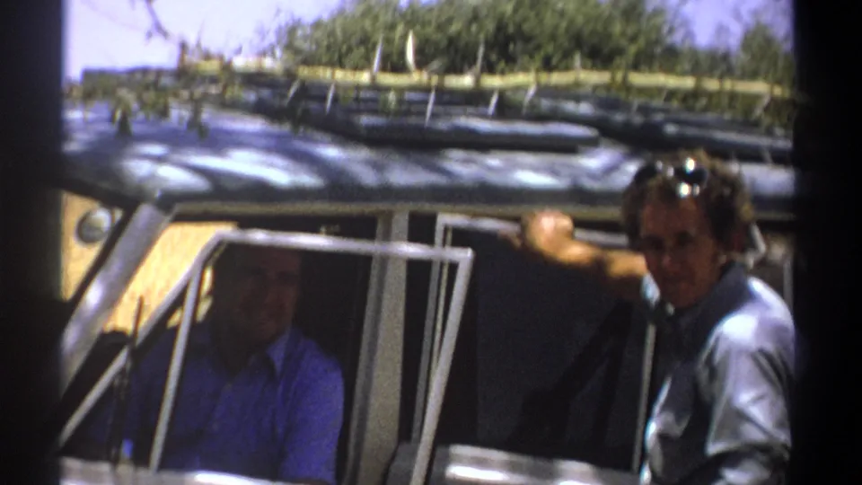 1969 Kenya 8mm frame showing a man leaning out near the vehicle door with roof-mounted branches or supplies above.