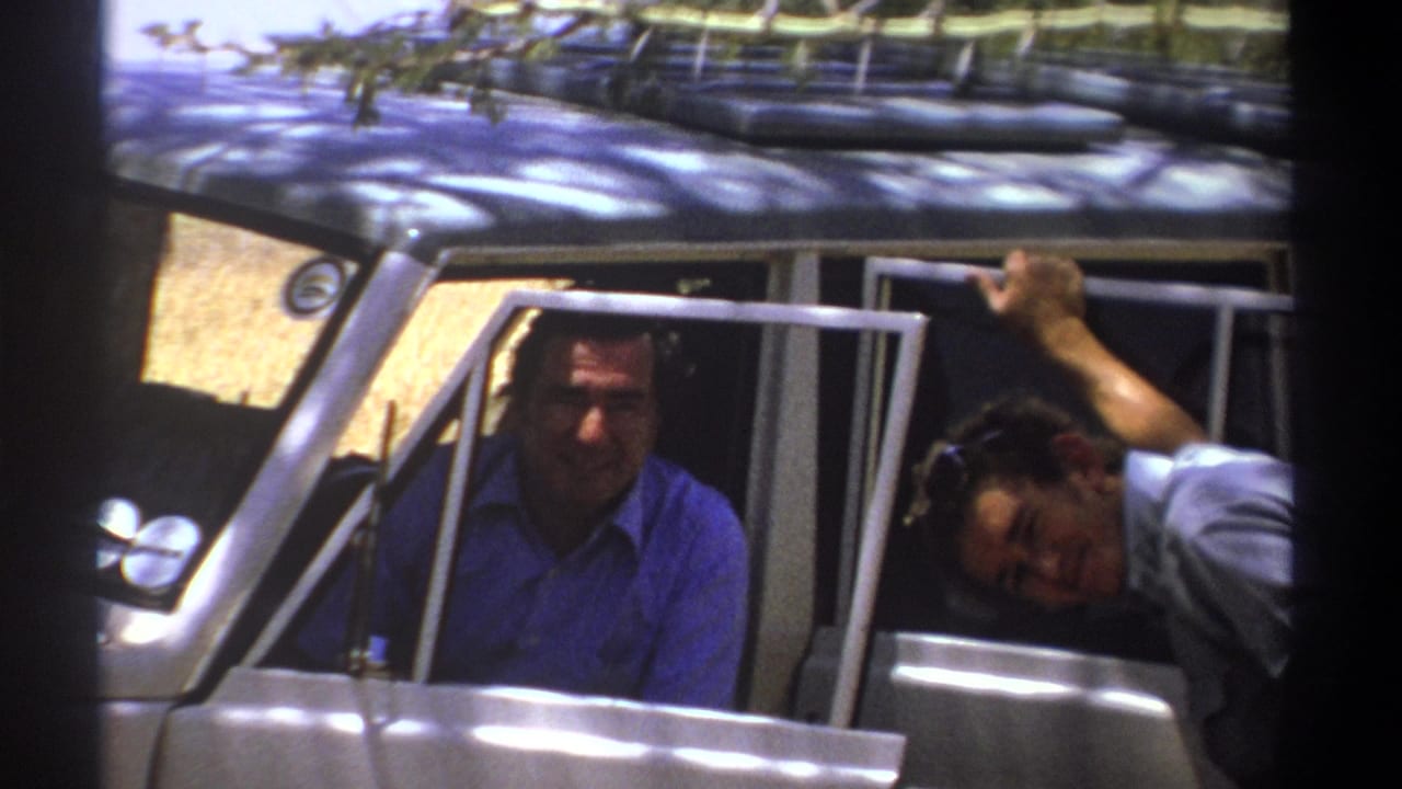 Man seated inside a vehicle while another man leans out smiling beside an open door.