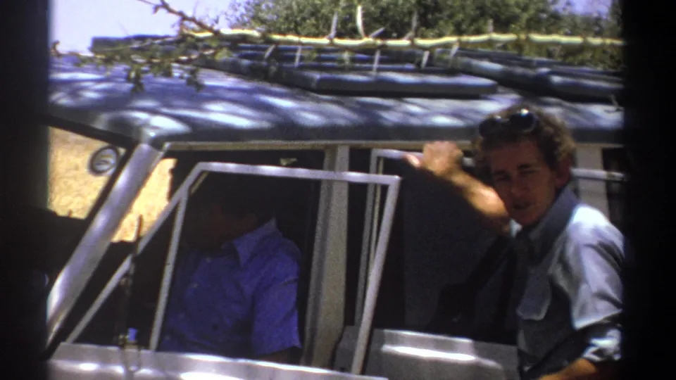 1969 Kenya frame showing a smiling man leaning beside an open vehicle door, with a second man partly visible inside.