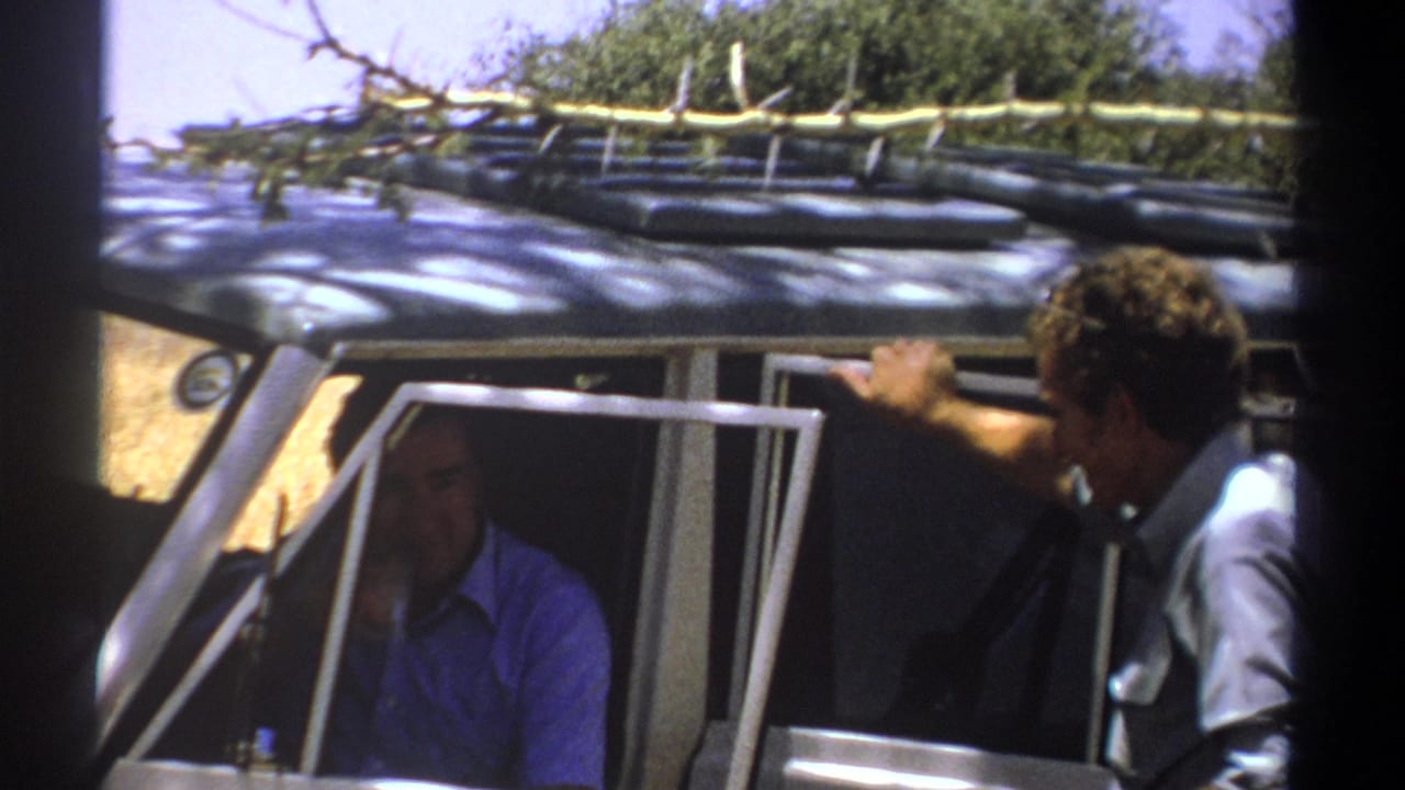 Man leans on an open vehicle window while another man sits inside.