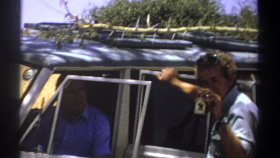 1969 Kenya travel frame with a man near the passenger window holding a small object close to his face.