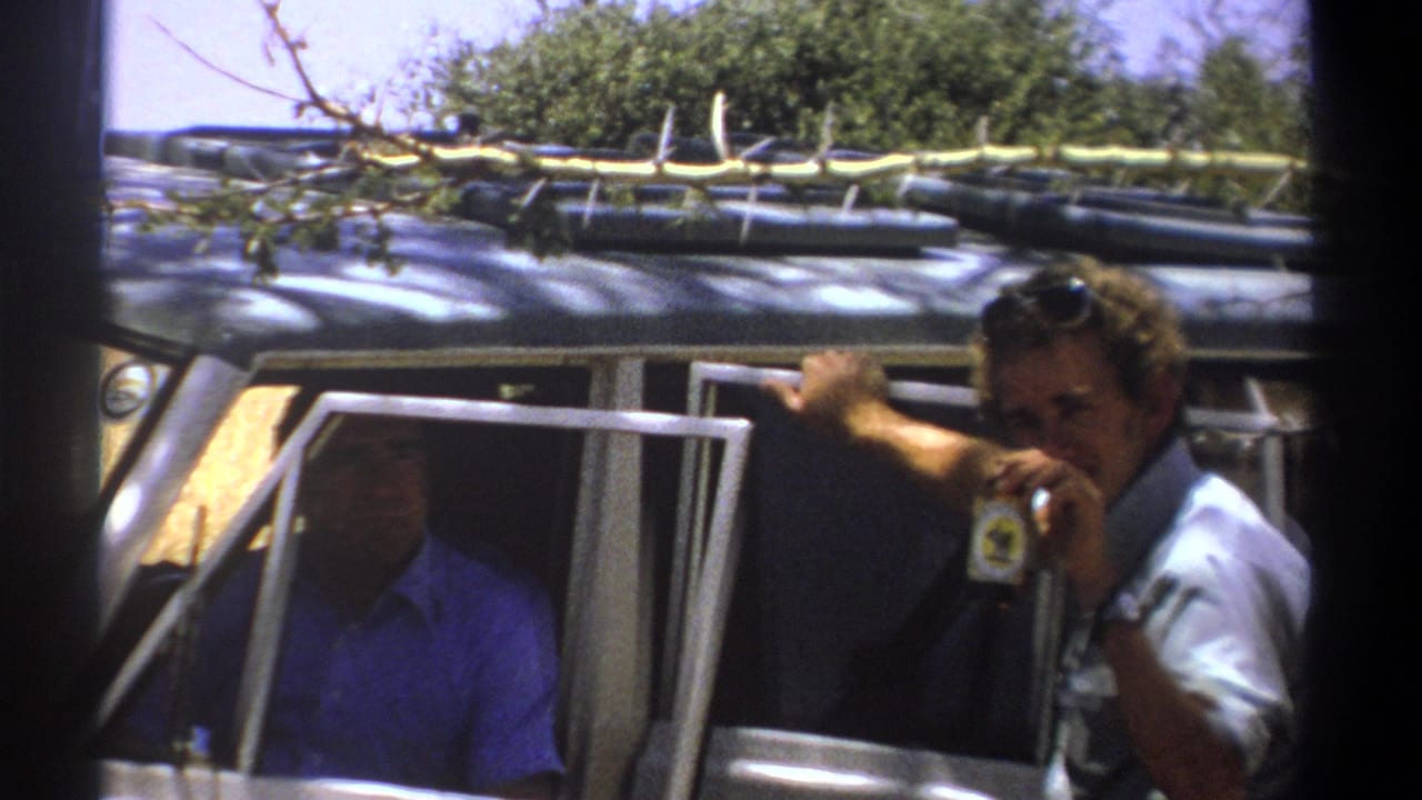 1969 Kenya safari home-movie frame showing a man in sunglasses leaning from a vehicle as another adult passenger sits inside.