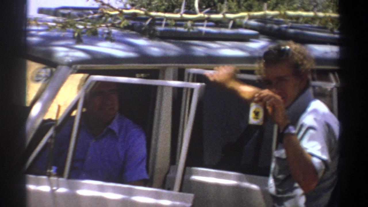 Man outside a safari vehicle holds up a small badge or tag.
