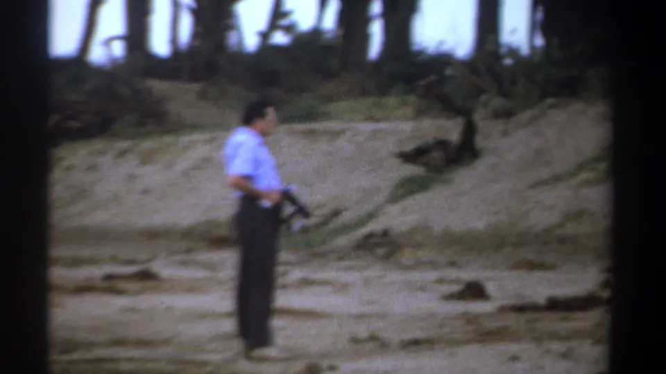 1969 Kenya 8mm frame showing a man in a light blue shirt holding a rifle near the hunting scene.