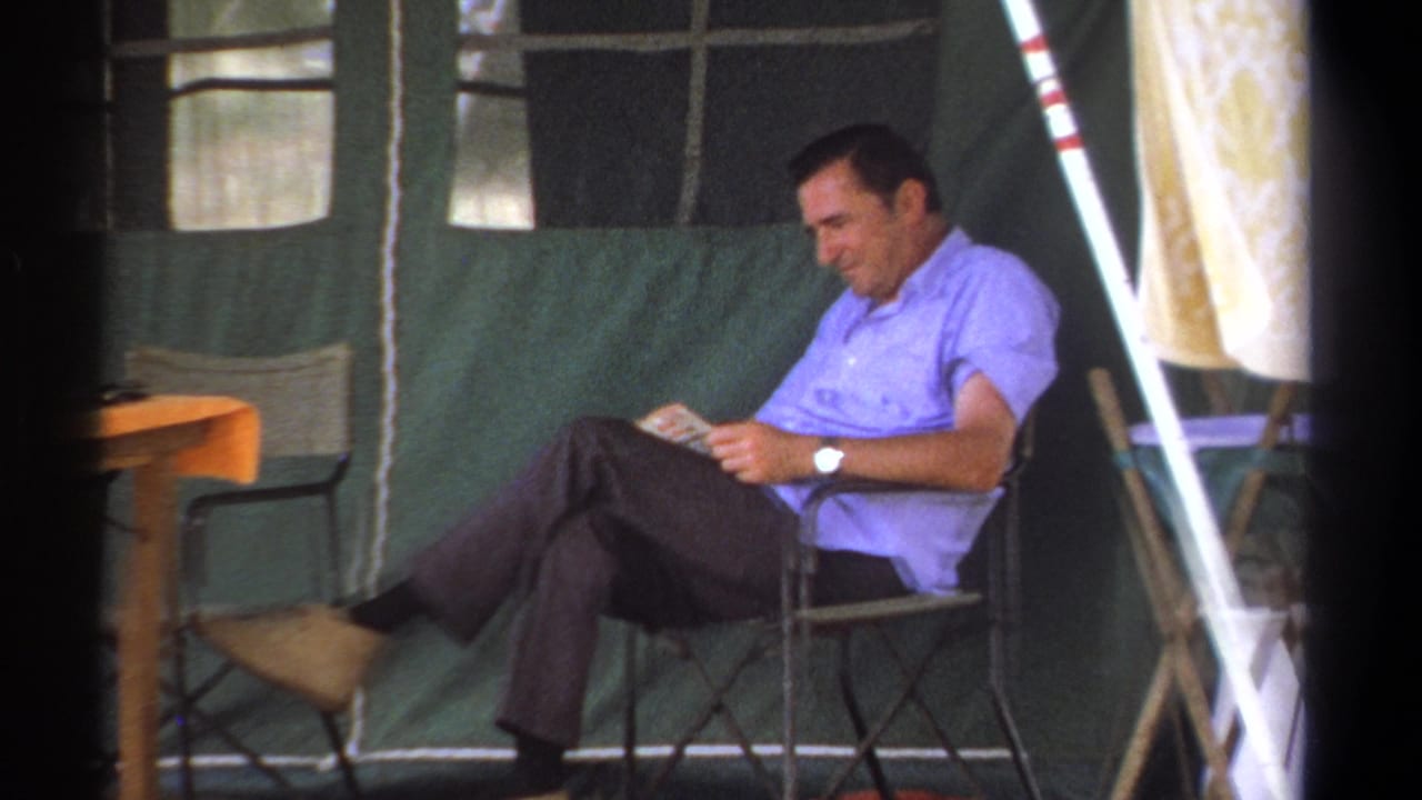 Man in a blue shirt reading beside a table inside a canvas tent.