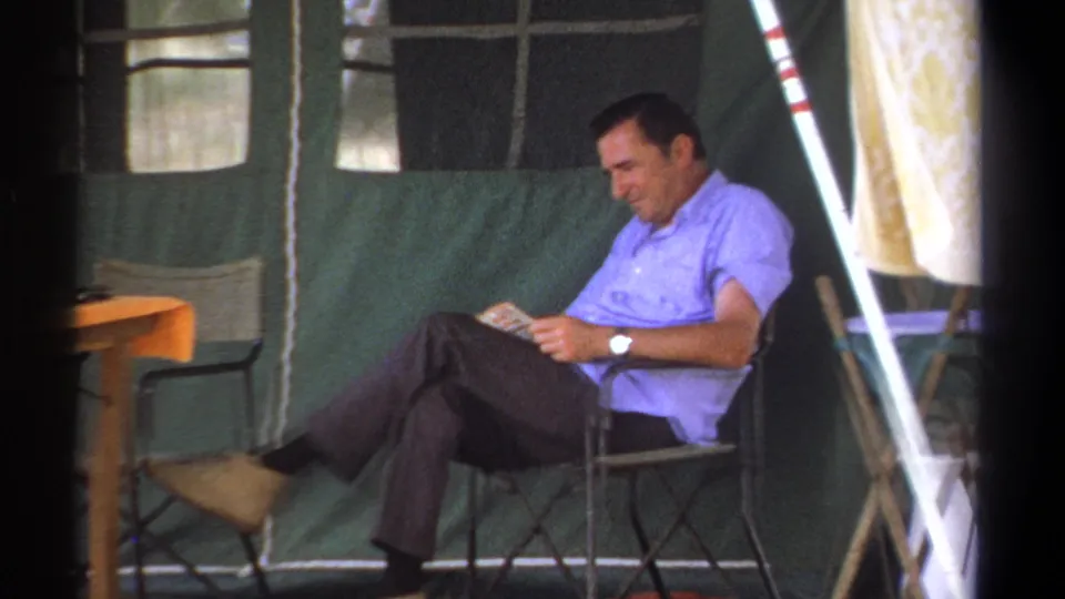 A seated man reads in a green canvas tent in Kenya, with a small table and tent windows visible around him.