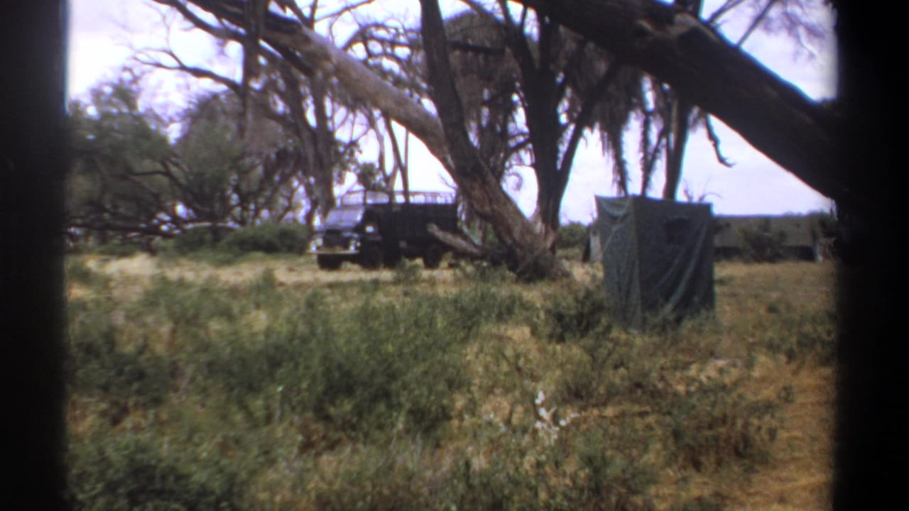1969 Kenya home-movie frame showing a blue-gray off-road van and green canvas shelter among dry grass and trees.