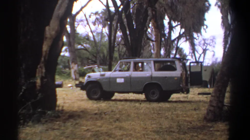 1969 Kenya 8mm frame showing the side of a parked gray station wagon, with a faint person visible inside the vehicle.