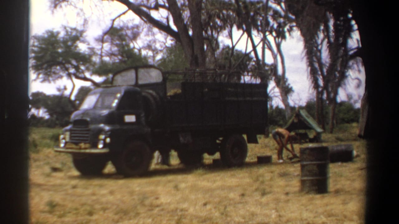 Dark green military truck in the 1969 Kenya camp scene, with scattered supplies and a small tent visible near the trees.