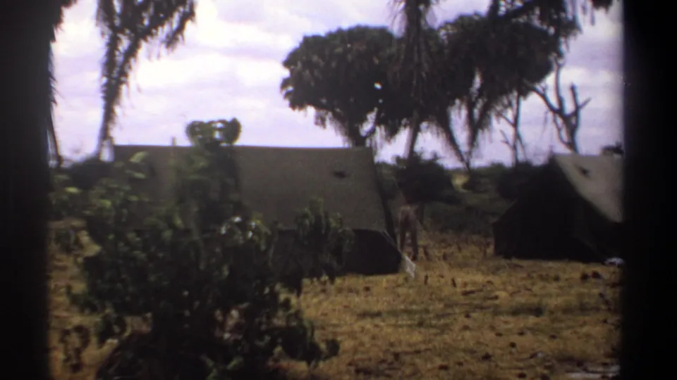 1969 Kenya 8mm frame with a large canvas tent in the foreground, palms and shrubs around it, and a second tent partly visible at the right edge.