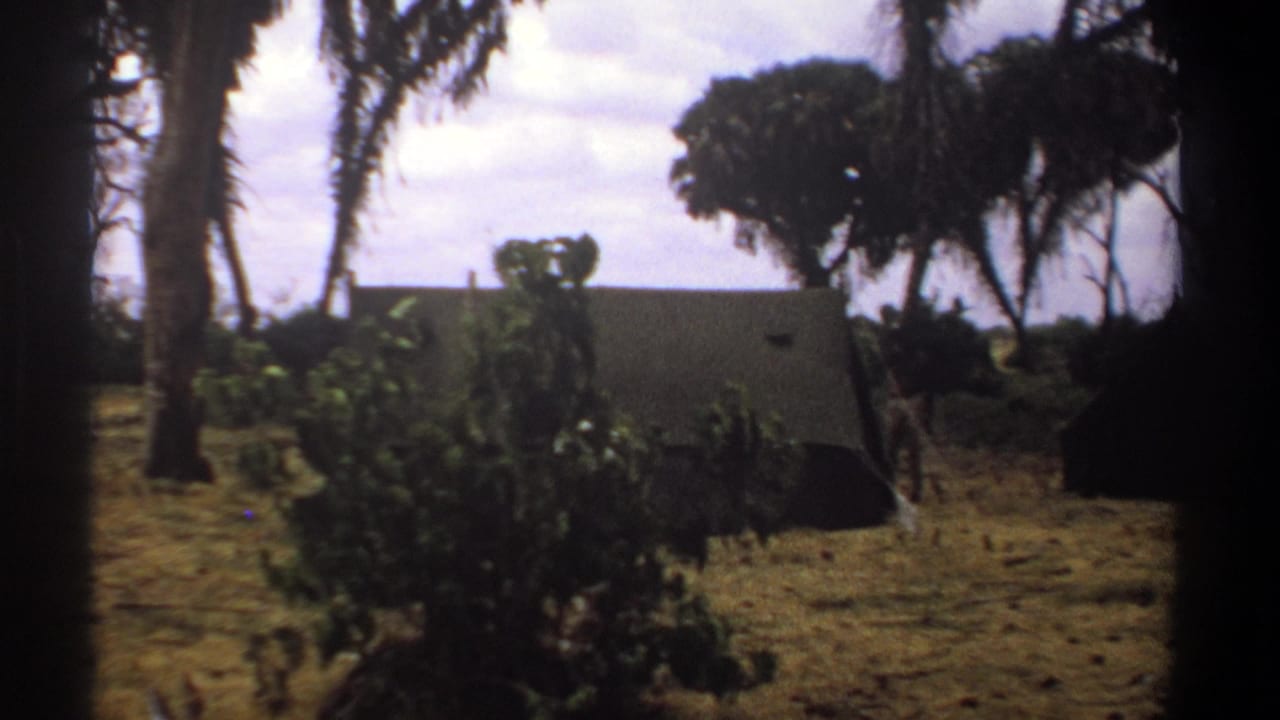 1969 Kenya 8mm frame showing a dry campsite with palms, shrubs, and canvas tents in the distance.