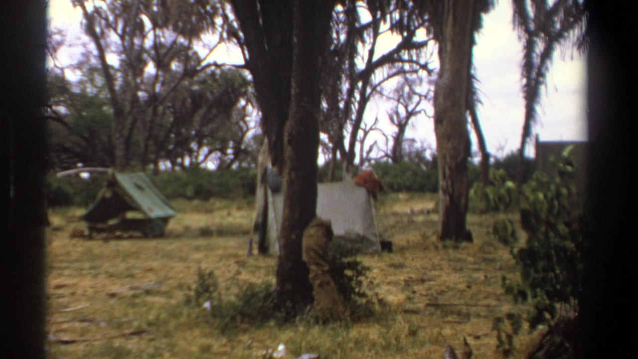 Kenya 1969 8mm frame showing small canvas tents in a wooded dry-grass camp area, with dark edges from the filming position.