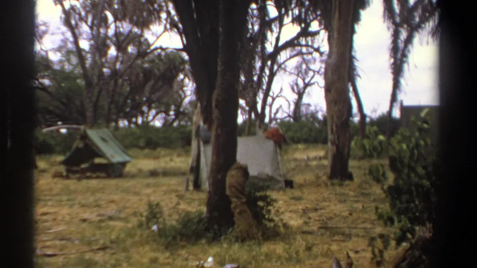 Kenya 1969 8mm frame showing small canvas tents in a wooded dry-grass camp area, with dark edges from the filming position.