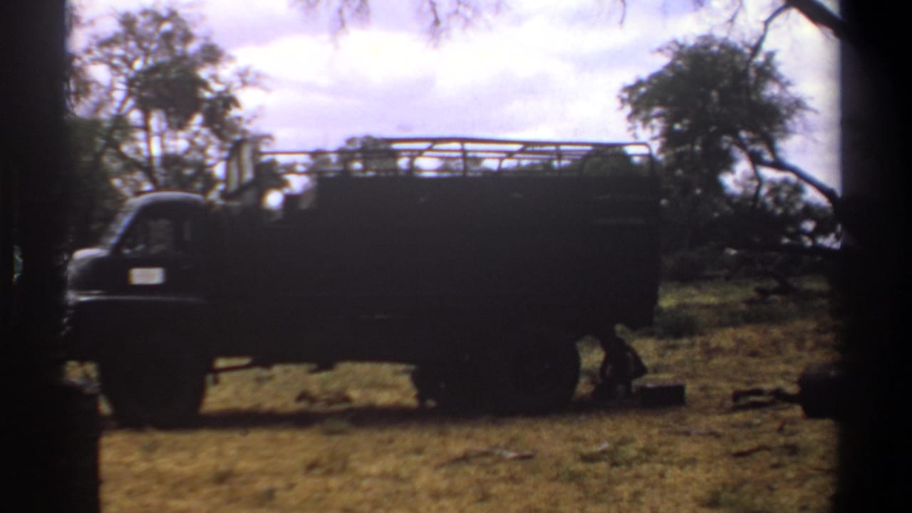1969 Kenya 8mm frame showing a dark truck in a rural clearing, with dry grass, trees, and heavy dark borders.