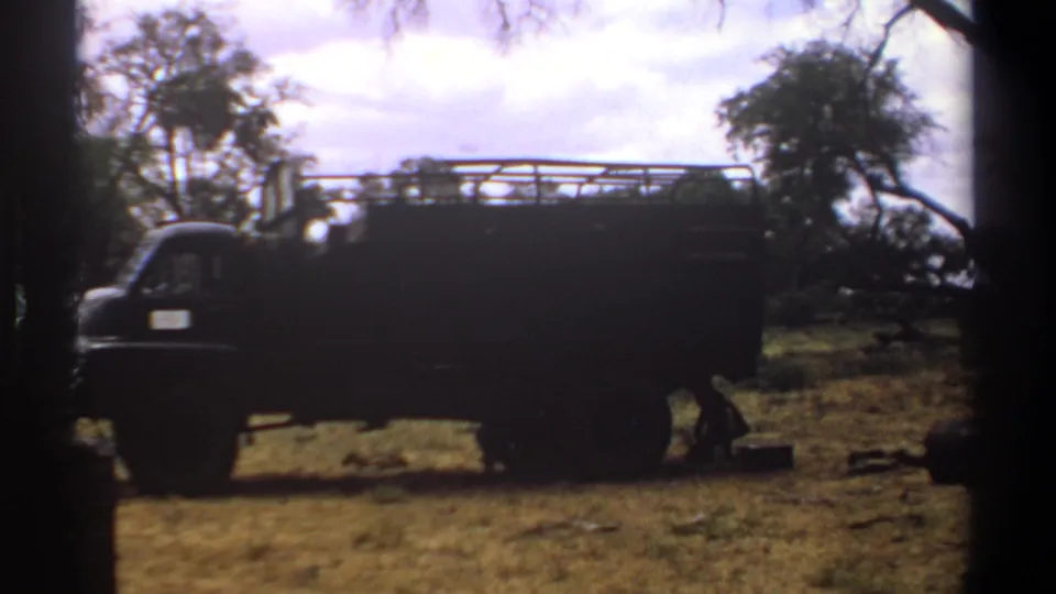 1969 Kenya 8mm frame showing a dark truck in a rural clearing, with dry grass, trees, and heavy dark borders.