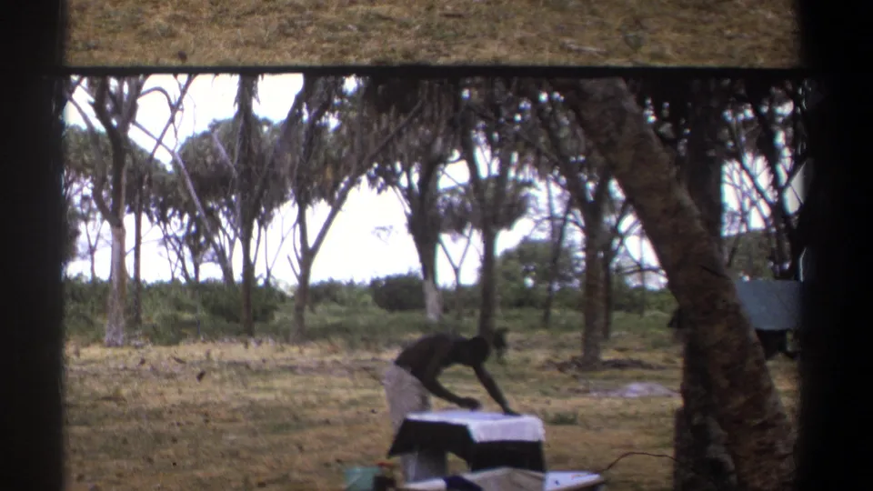 In the lower-left frame, the man bends close to the table while handling or cleaning an object in the same wooded grassy setting.