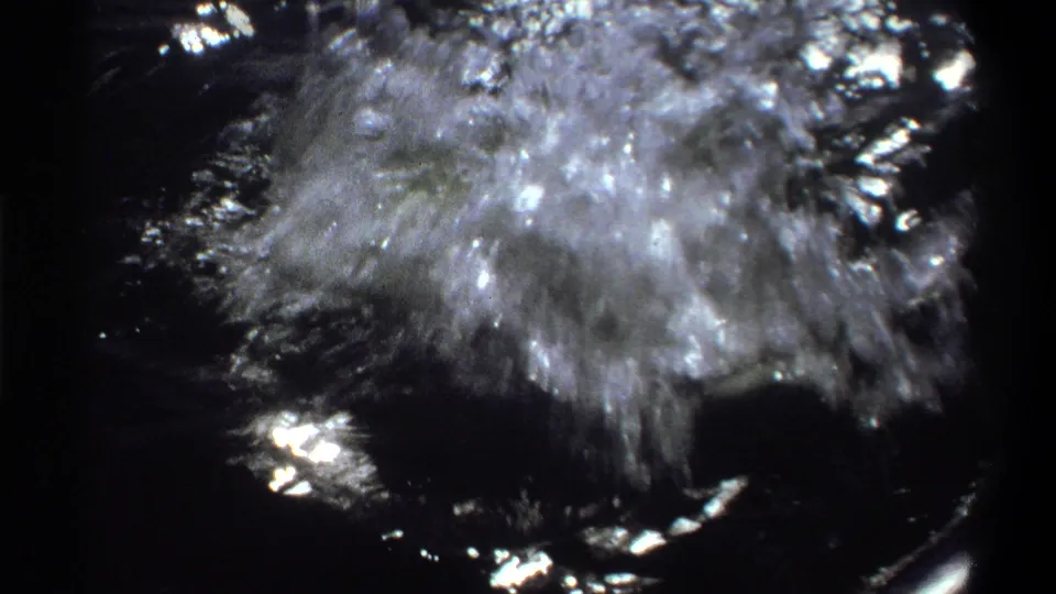 1969 Nigeria 8mm frame showing a fish breaking the water in a burst of spray beside a small boat.