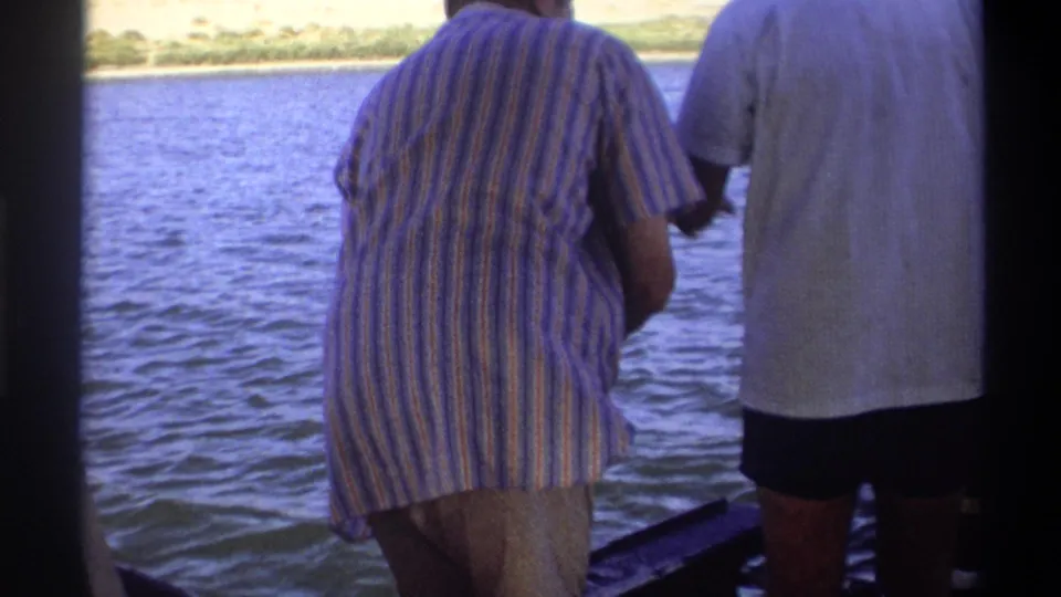 Two adult men in casual shirts stand at a boat rail on a Nigerian waterway, consistent with supplied 1969 home-movie metadata.