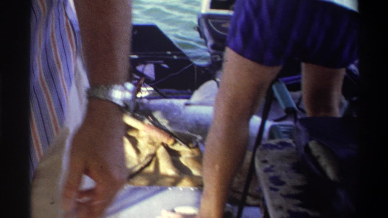 1969 Nigeria 8mm frame showing adults' legs in a small boat with a large fish on deck and water visible beyond the rail.