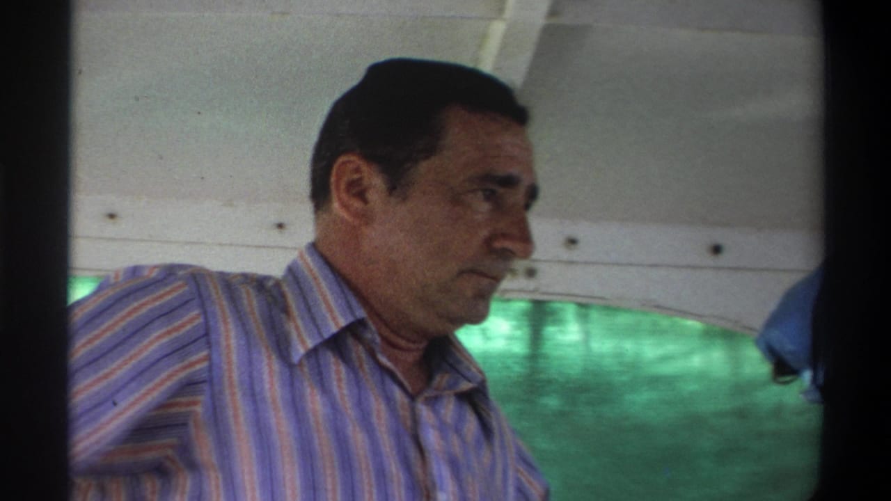 1969 Nigeria 8mm frame showing an adult man in a striped shirt under a boat canopy, with green water visible through the side opening.