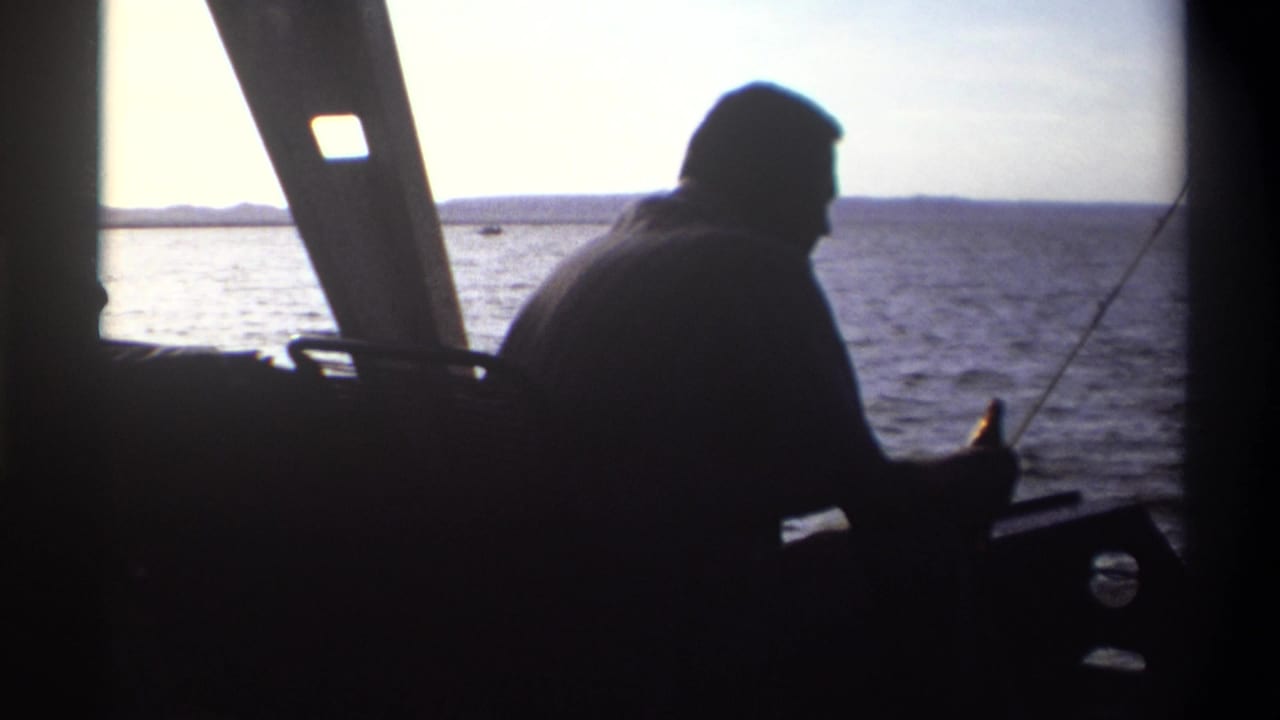 1969 Nigeria 8mm frame showing a silhouetted man seated in a boat with a fishing pole, backlit by bright open water.