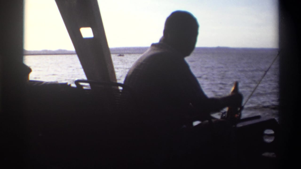 1969 Nigeria 8mm frame of a man in silhouette seated on a boat, with fishing pole, window frame, water, and horizon behind him.